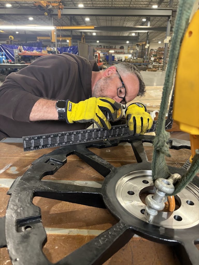 An Alloway builder measuring a cast wheel on the shop floor in Fargo